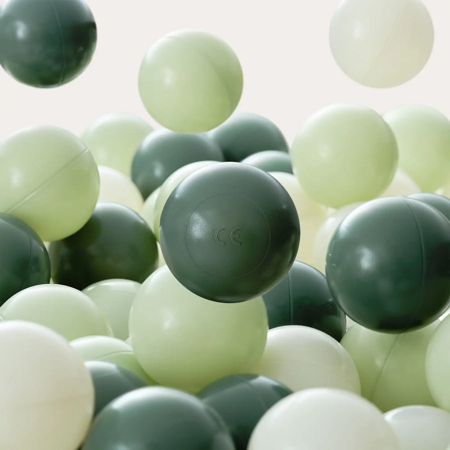A close-up of Tiny Land® Ocean Ball - 200 pcs with Varied Colors by Tiny Land shows non-toxic balls in dark green, light green, and white. A dark green ball featuring the CE marking is prominently placed at the center.|Green