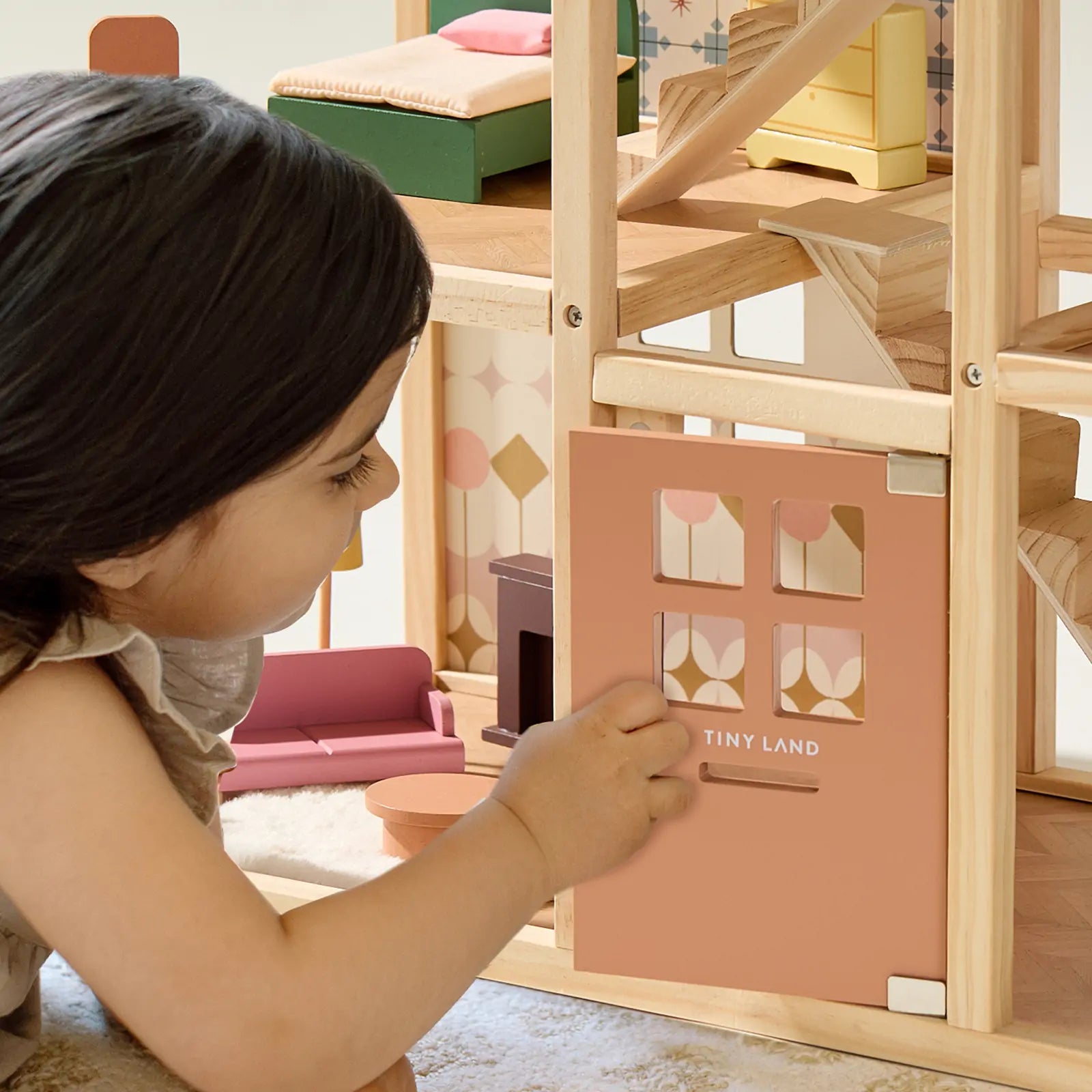 A young child opens the Tiny Land® Sweetwood Pegasus Dollhouse, unveiling miniature furniture, charming rooms, and poseable wooden dolls from Tiny Land inside.