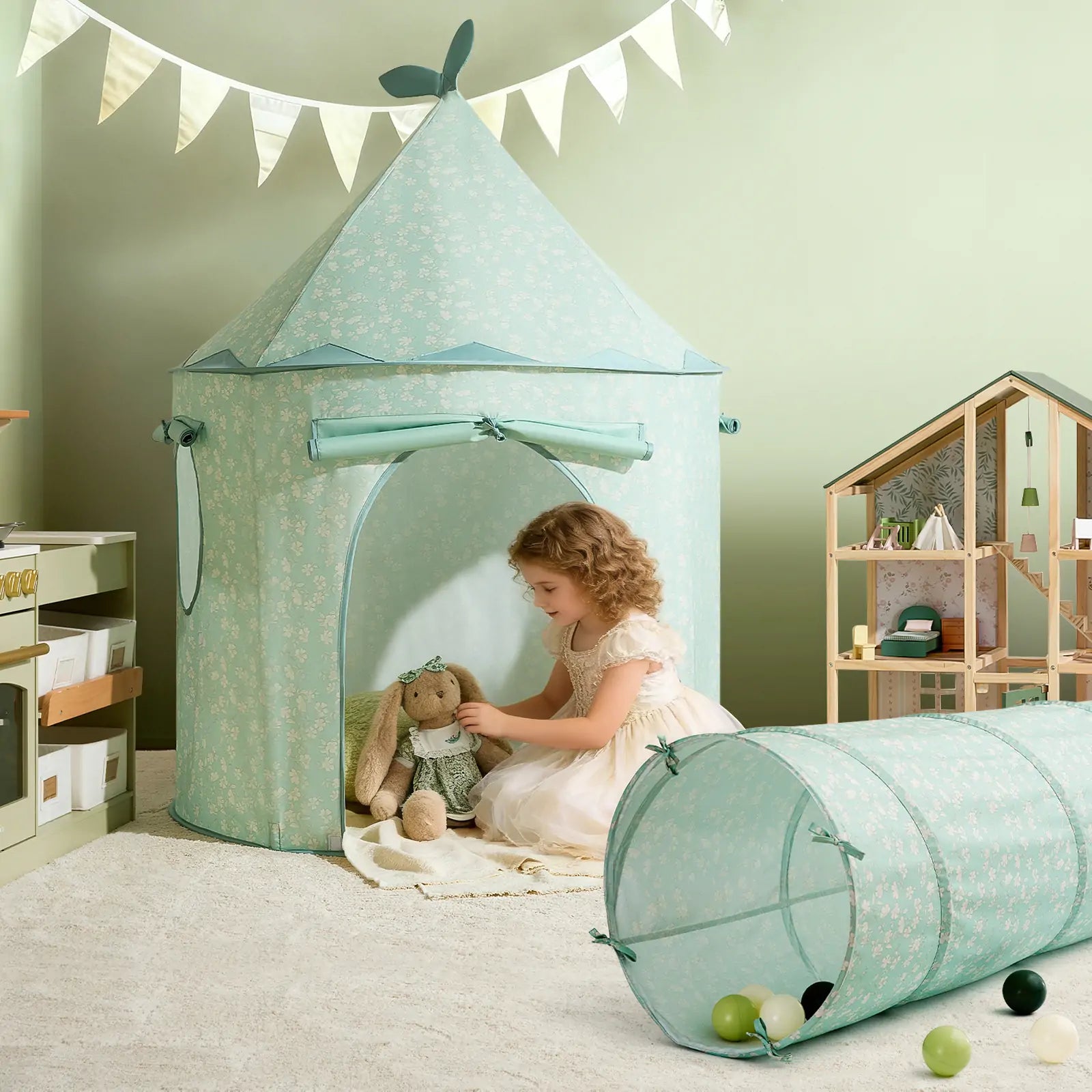 A young girl in a white dress sits in a mint green play tent, holding a stuffed bunny. The pastel-themed room includes the Tiny Land® Adventure Play Tunnel - Green, a dollhouse, and a banner on the wall.|green