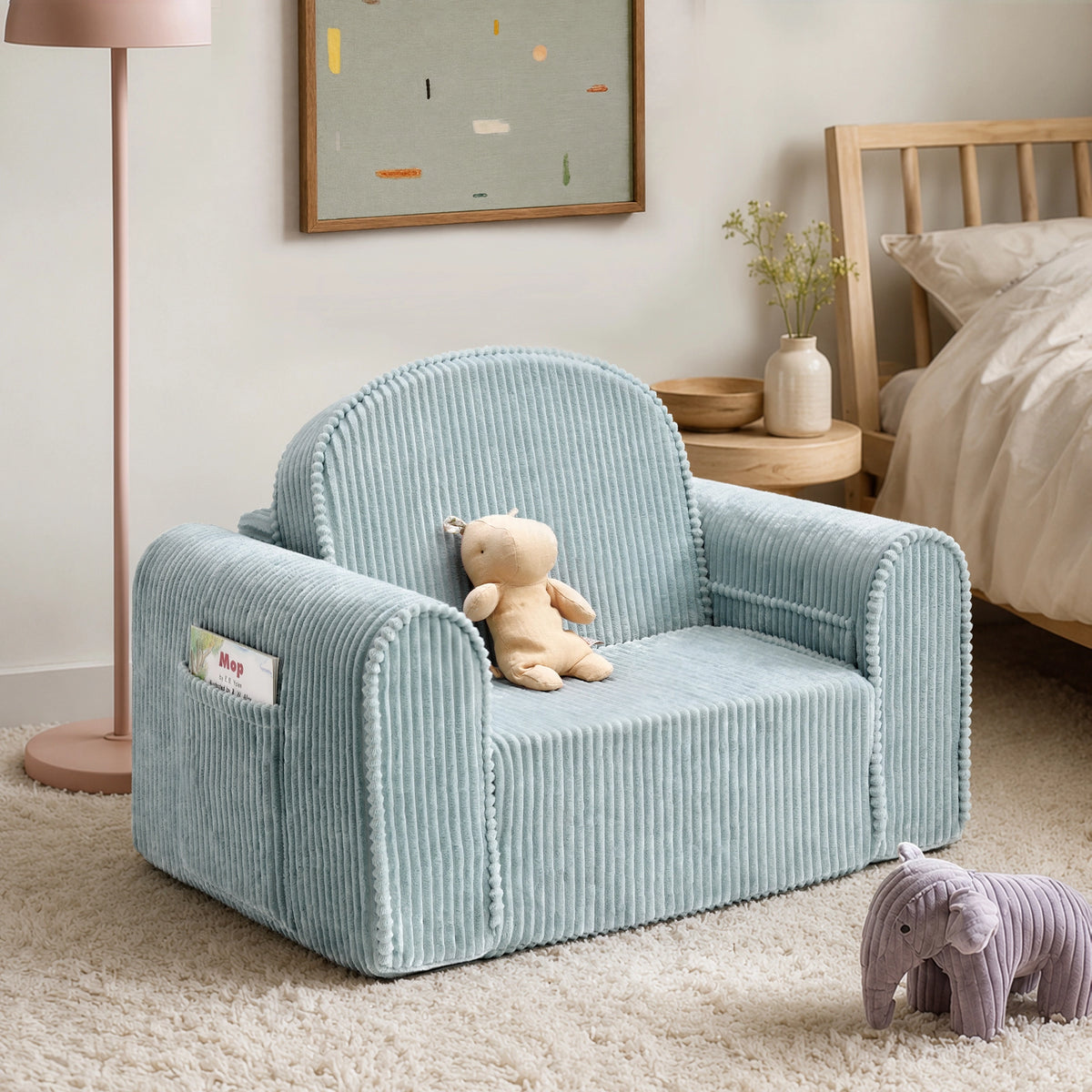 A Tiny Land® GentleSnug Corduroy Kid Chair in light blue sits on a beige rug in a child’s room, with a plush bear placed on the seat and a stuffed elephant on the floor. In the background, there is a framed abstract artwork and a pink lamp.|Soft Teal