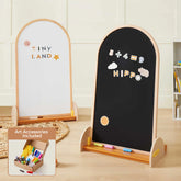 Two wooden-framed easels—a whiteboard on one side and a blackboard on the other—stand side by side with colorful chalk. The Tiny Land® Double-Sided Arched Magnet Chalkboard & Art Kit is perfect for young artists, and an inset shows the included kids' art accessory kit featuring markers, erasers, and chalk from Tiny Land.