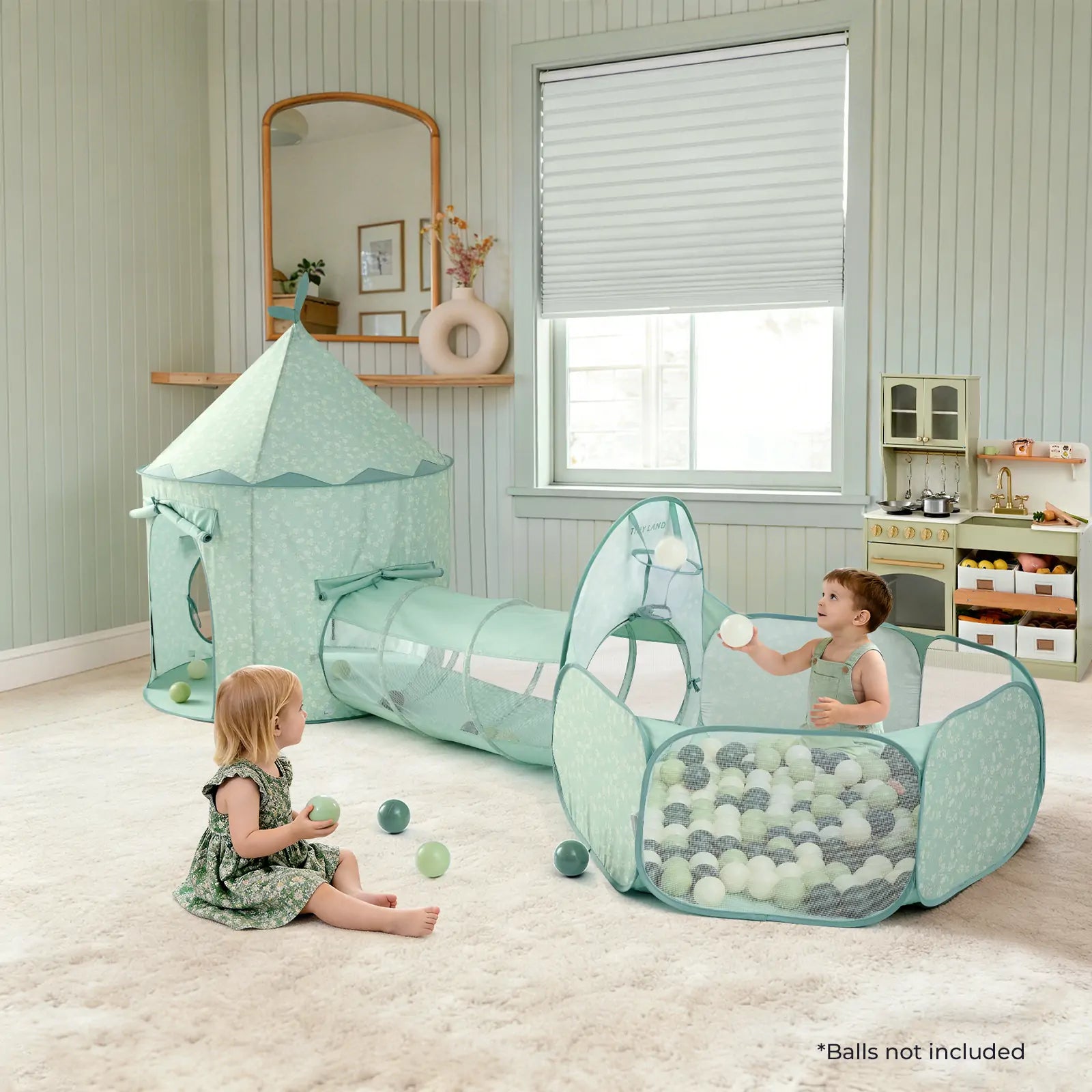 Two young children play in the Tiny Land® Compact Adventure 3-in-1 Play Tunnel With no Balls – Green by Tiny Land. The light green tent, attached tunnel, and ball pit sit on a soft carpet in a bright room with toys and colorful balls scattered around.