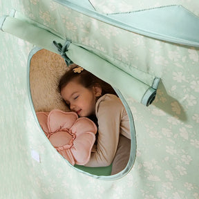 A young girl sleeps peacefully inside the Tiny Land® Tiny Sprout Castle Tent, holding a pink flower-shaped pillow and resting her head on a beige cushion.