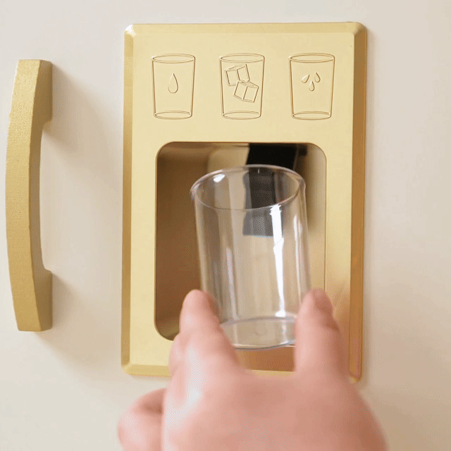 A hand holds a glass of colorful candies under the Tiny Land® PopJoy Play Kitchen fridge dispenser, where water and ice icons are shown above, blending playful imagination with realistic kitchen features.