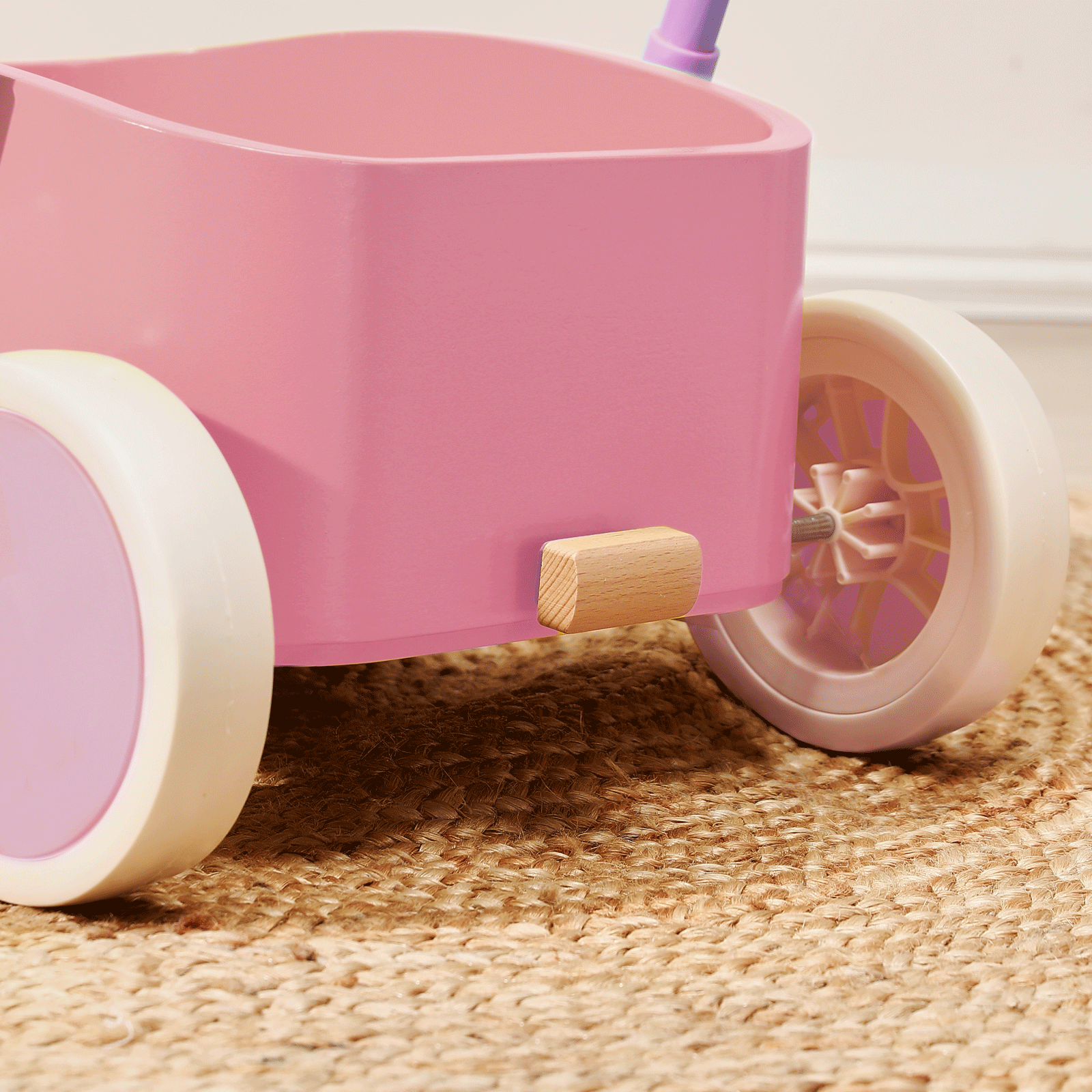 A close-up of the Tiny Land® 3-in-1 Wooden Baby Walker Wagon in pink, featuring large white and pink wheels, sits on a woven beige rug indoors.