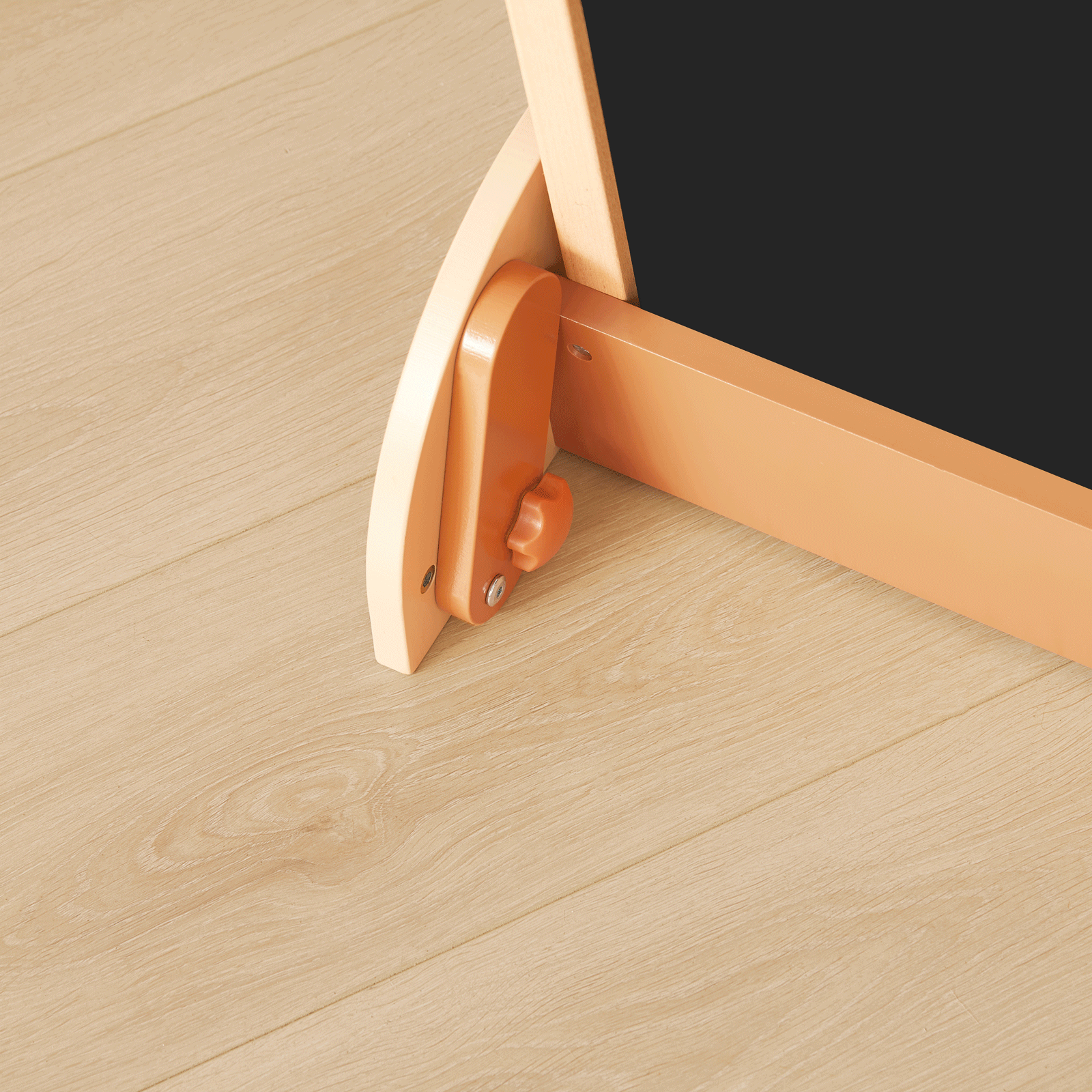 Close-up of a Tiny Land® Double-Sided Arched Magnet Chalkboard's beechwood easel leg with adjustable knob on a light wood floor. The corner of the Tiny Land kids whiteboard chalkboard is visible at the top right.