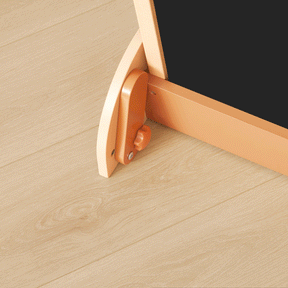 Close-up of a Tiny Land® Double-Sided Arched Magnet Chalkboard's beechwood easel leg with adjustable knob on a light wood floor. The corner of the Tiny Land kids whiteboard chalkboard is visible at the top right.