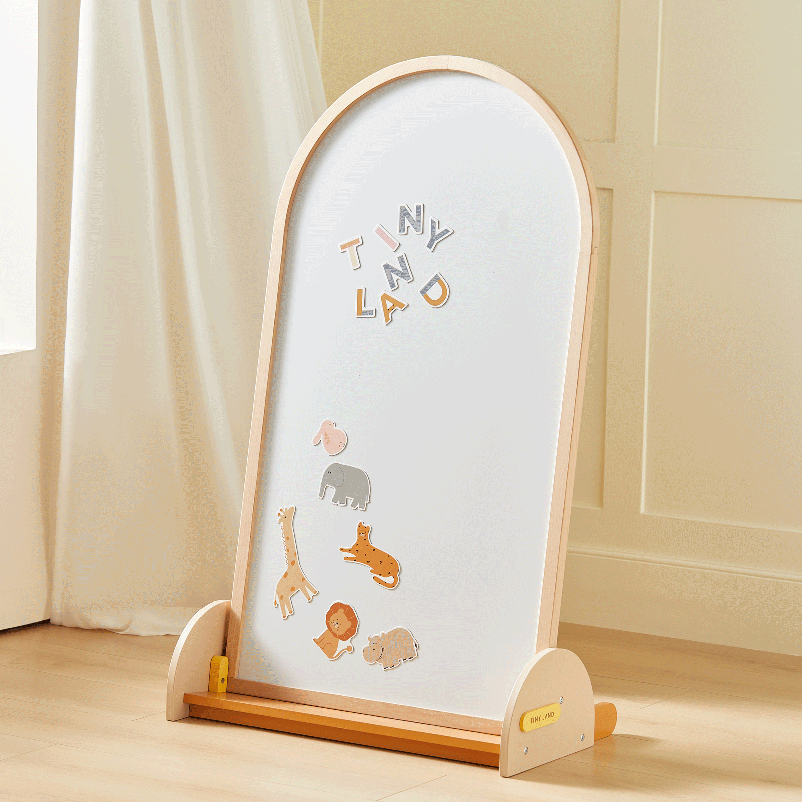 The Tiny Land® Double-Sided Arched Magnet Chalkboard stands on a light wood floor, decorated with magnetic letters spelling TINY LAD and animal magnets—a giraffe, lion, and elephant—by Tiny Land.