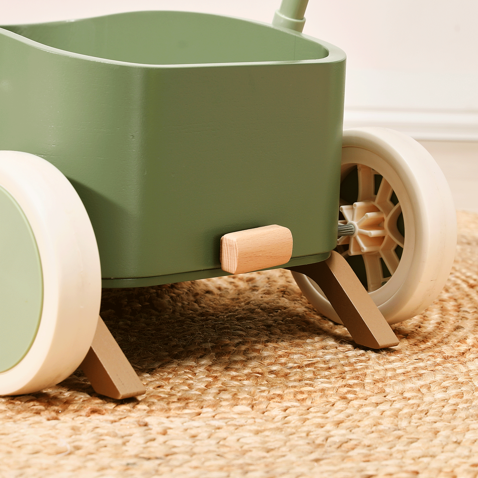 Close-up of the Test Tiny Land® JoyRide Baby Walker with Blocks in sage, featuring white wheels, wooden accents, adjustable speed control, shown on a woven jute rug.