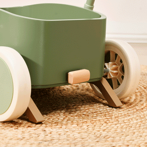 Close-up of the Test Tiny Land® JoyRide Baby Walker with Blocks in sage, featuring white wheels, wooden accents, adjustable speed control, shown on a woven jute rug.