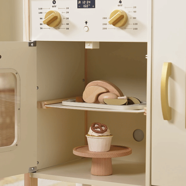The Tiny Land® PopJoy Play Kitchen oven, designed by Tiny Land, features cream and gold details and comes with wooden toy food: a tray of bread on the middle shelf and a cupcake with a pretzel topper on the bottom—ideal for any kids play kitchen.