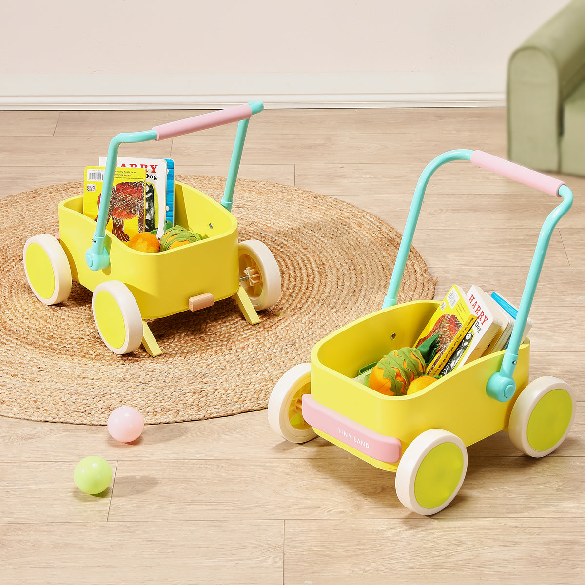 Two yellow Tiny Land® 3-in-1 Wooden Baby Walker Wagon - Pink & Spring Color units with light blue and pink handles, filled with children’s books and toy fruits, sitting on a round woven rug.|Spring Color