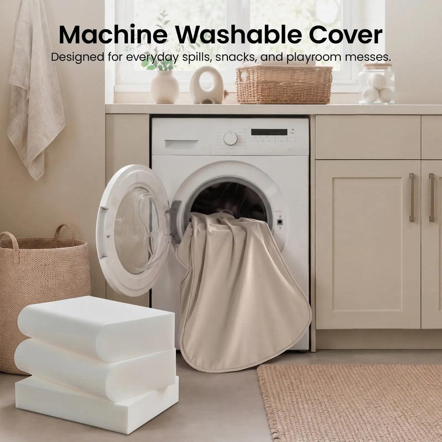 A beige fabric cover from the Tiny Land® GentleSnug Kid Chair is being placed into a front-loading washing machine in a neutral-toned laundry room. Text above reads: Machine Washable Cover. Designed for everyday spills, snacks, and playroom messes—perfect for children’s lounge chairs and playroom furniture by Tiny Land.|Beige