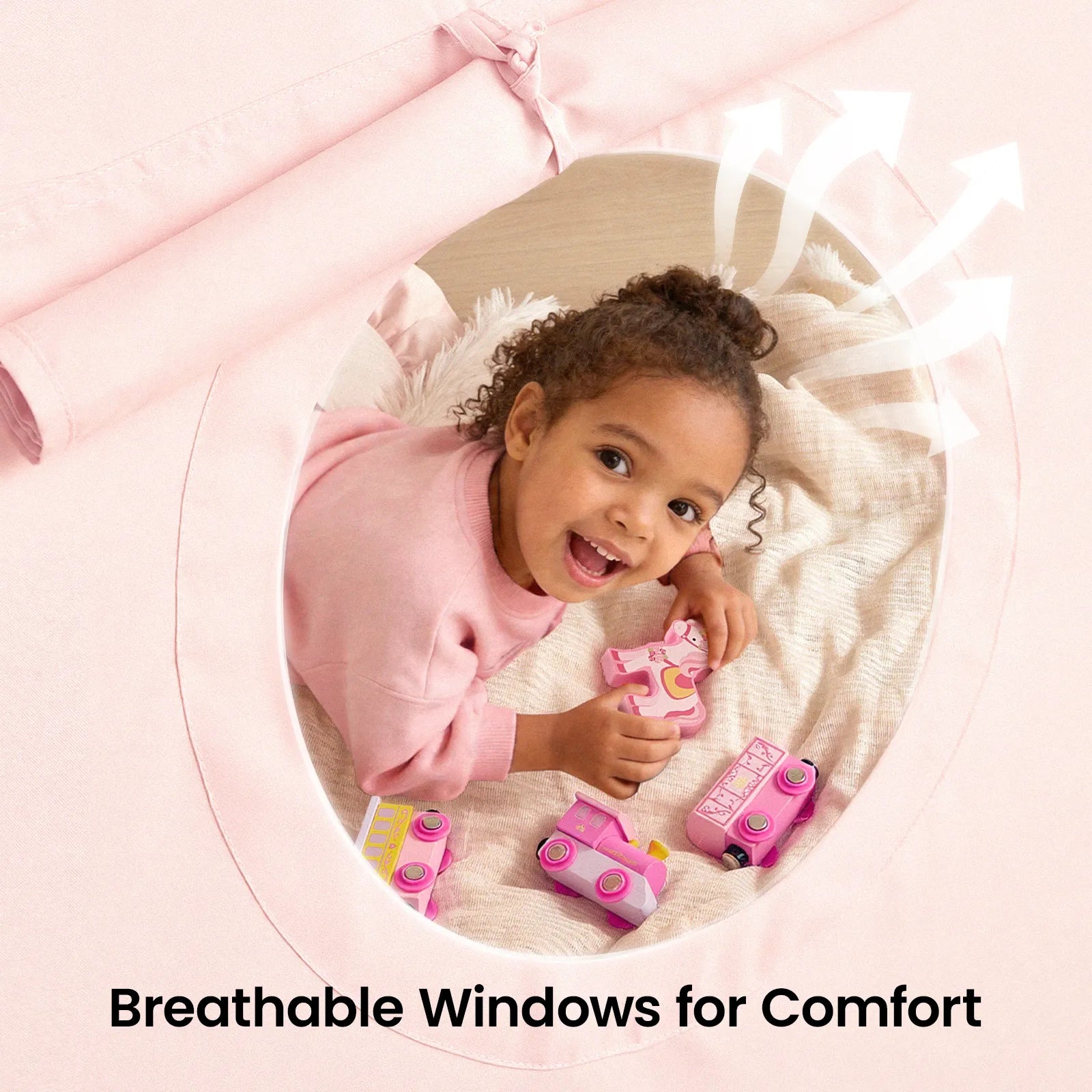 A young child smiles inside the Tiny Land® Kids Bed Tent, playing with pink toy vehicles near its round breathable window. White arrows show airflow. Text reads: Breathable Windows for Comfort.|Pink