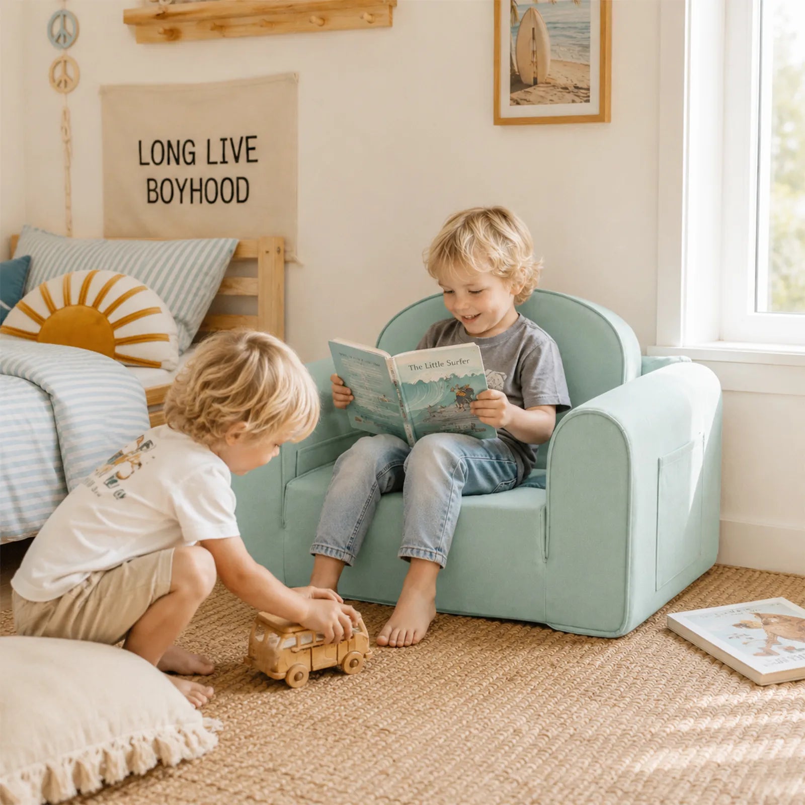 Two young boys play in a sunlit room. One sits in a Tiny Land® GentleSnug Kids Sofa Chair reading a book, while the other plays with a toy car on the floor. The space features playful, beach-themed decor.