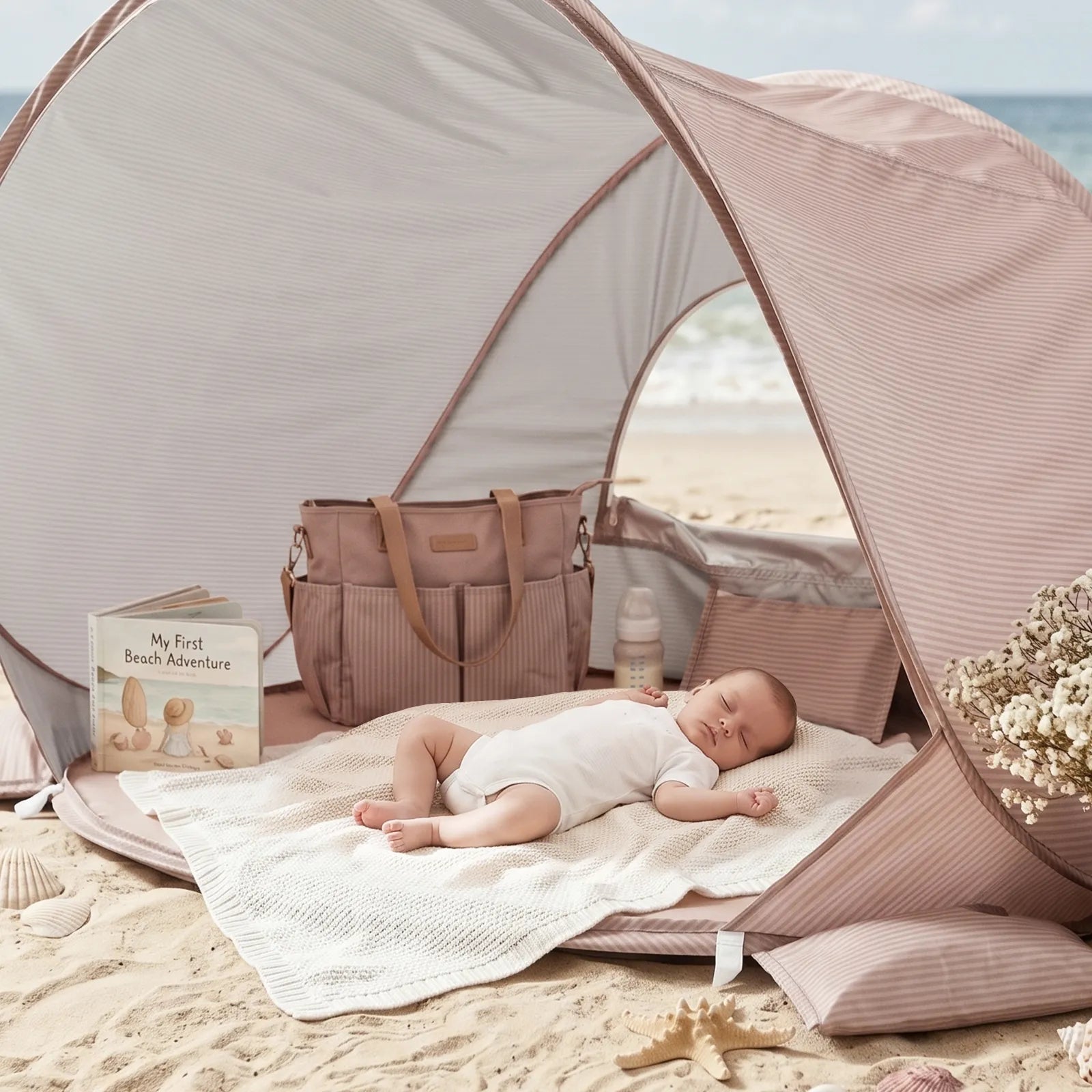 A baby naps on a white blanket inside the Tiny Land® 4-in-1 Baby Beach Tent & Sand Toy Set by Tiny Land on the sand, with a diaper bag, bottle, flowers, and a “My First Beach Adventure” book nearby. The sea and sky are visible in the background.|Pink