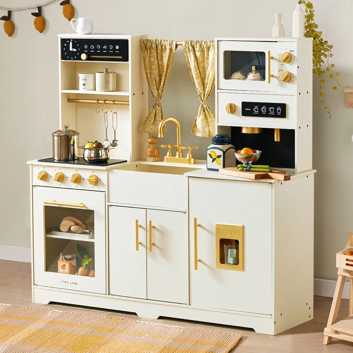 The Tiny Land® Iconic Wooden Play Kitchen – Cream Pretend Cooking Set for Kids by Tiny Land features a cream and gold design with a toy stove, sink, microwave, and utensils. Pretend play kitchen food and accessories are neatly arranged on the countertop and shelves, while gold curtains decorate the window above the sink.