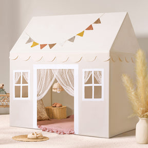 The Tiny Land® Playhouse Tent – Natural Cream Indoor Tent for Kids by Tiny Land features scalloped trim, window designs, lace curtains, and a fabric bunting, set on a soft rug with pampas grass and a basket in a cozy, sunlit room.
