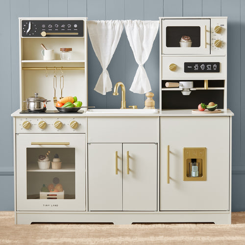 The Tiny Land® Play Kitchen with Running Water - Iconic Aqua Kitchen in Cream by Tiny Land features an oven, stovetop, sink, microwave, fridge, play food, utensils, pots, and veggies. White curtains and a gray wall add realistic fun for kids.