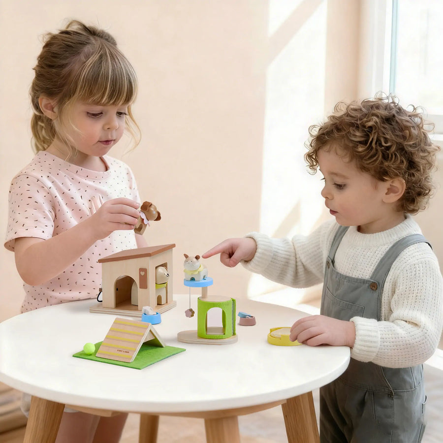 Two young children enjoy creative pretend play at a round white table with the Tiny Land® Happy Urban Paws set by Tiny Land, featuring a mini house, ramp, and pet figurines in a bright, sunlit room.