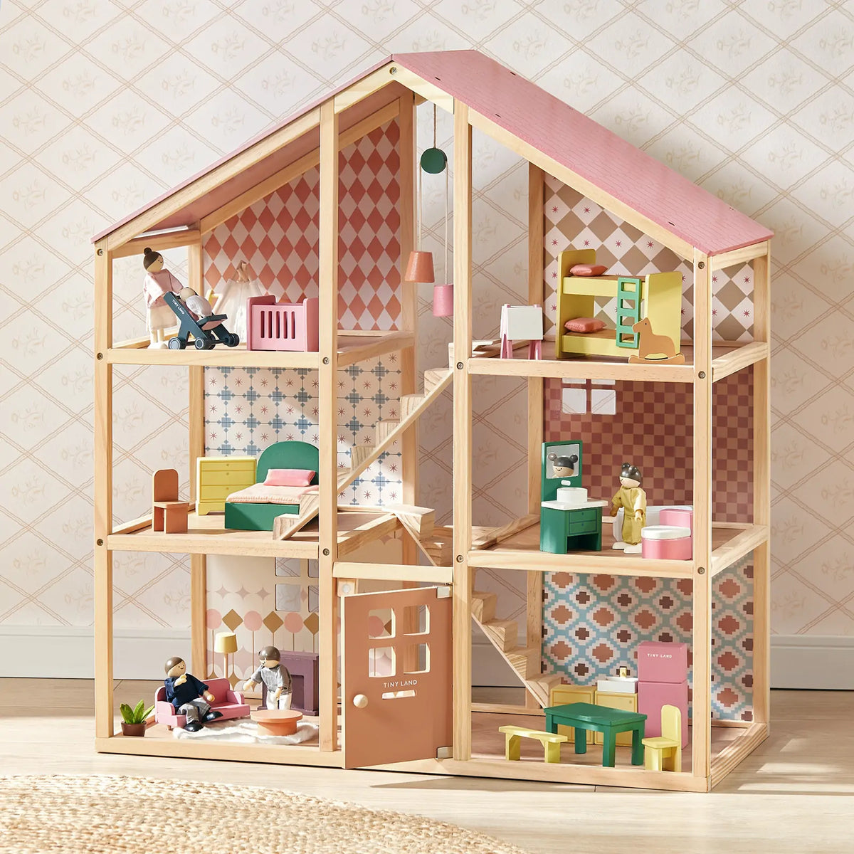 The Tiny Land® Sweetwood Pegasus Dollhouse & Wooden Dollhouse Dolls by Tiny Land features six rooms, colorful wallpaper, a pink roof, furniture like beds and tables, and poseable dolls arranged throughout for imaginative play.