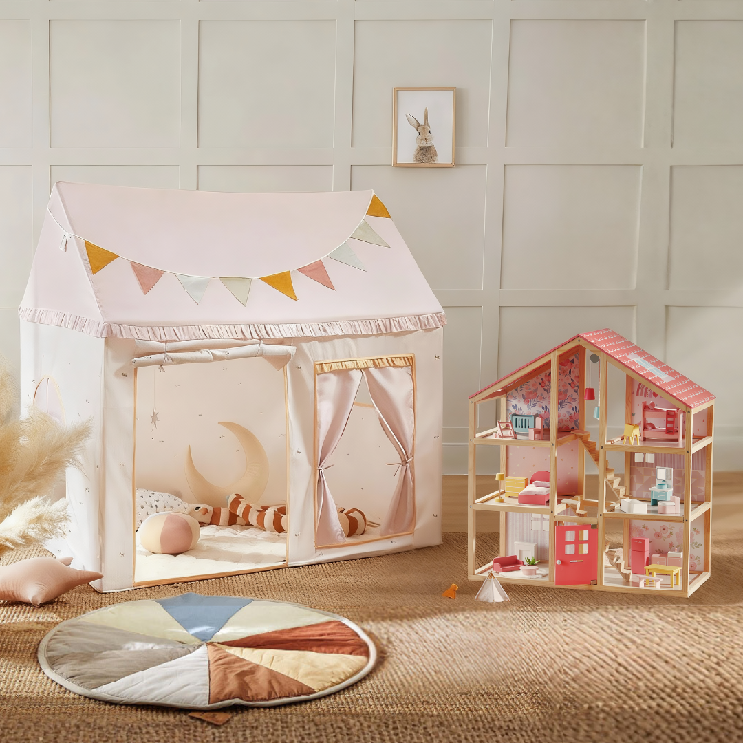A cozy playroom showcases the Tiny Land Sweet Dreams Playset—featuring a pink-white playhouse and a pink dollhouse—set on a round rug, inspiring imaginative play against a white panel wall.