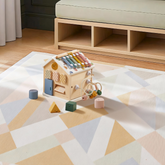 The Tiny Land Cozy Learning Playset — Playmat + Activity Cube is placed on a geometric-patterned rug in a cozy room with wood floors and a low bench, with shaped blocks scattered around this colorful developmental toy.