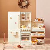 The Tiny Land Food-Filled Kitchen Gift Set features cream cabinets, toy fridge, oven, sink, and shelves. Pumpkins, leaves, produce baskets, a pink candle, and a wreath add festive autumn charm to this play kitchen.