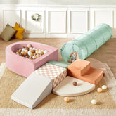 The Tiny Land® PlayNest Climbing Ball Pit Set with Tunnel by Tiny Land features a pastel indoor playground, including a pink foam ball pit with multicolored balls, climbing blocks, green tunnel, orange steps, and cushions on a beige rug.