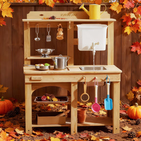 The Tiny Land® Mud Kitchen - DuoPlay Outdoor Play Kitchen for Kids by Tiny Land is set outdoors in autumn, with toy utensils, pots, pans, a yellow watering can on top, plus colorful leaves and small pumpkins for perfect sensory play.