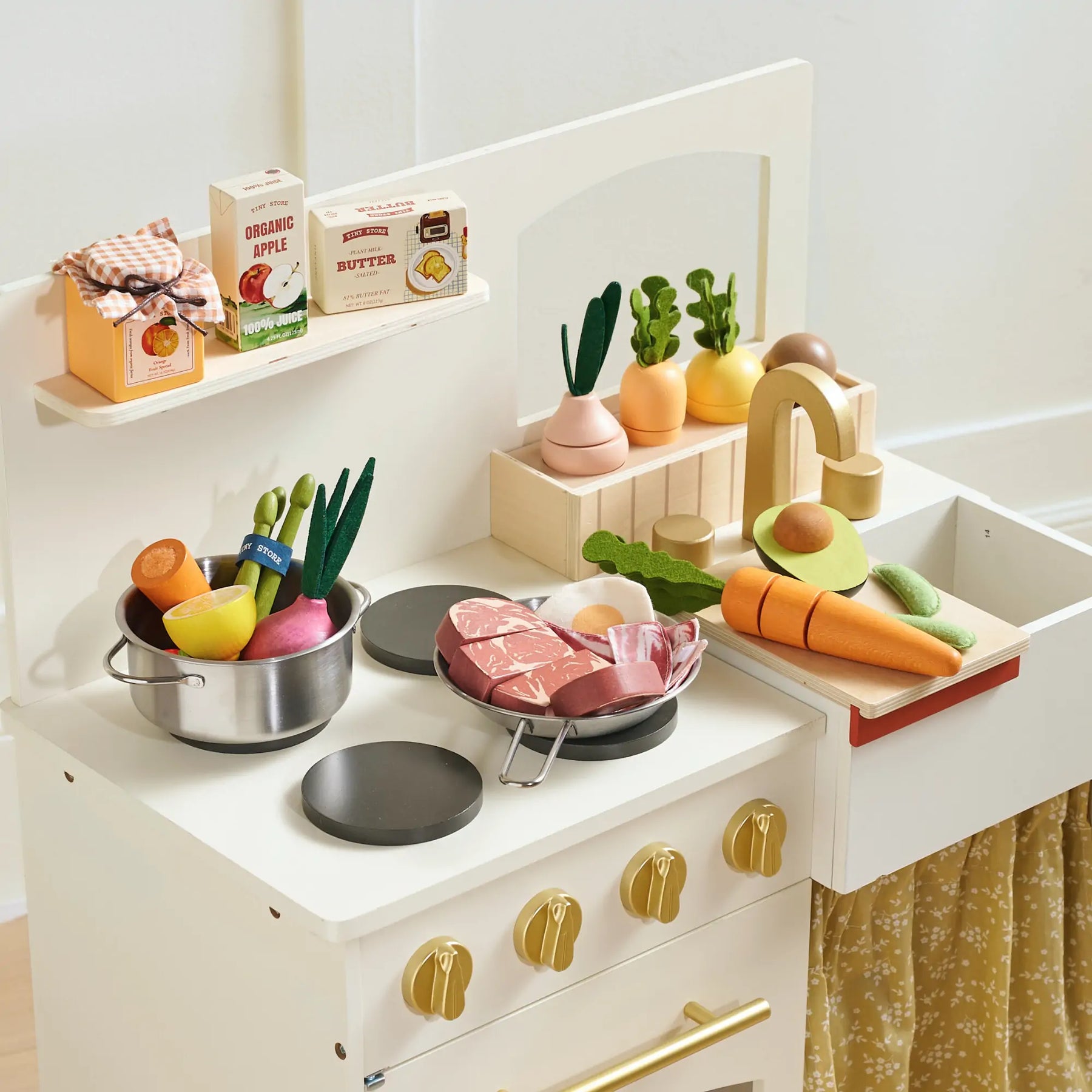 The Tiny Land® Organic Meat & Seafood Pack by Tiny Land is displayed on a white countertop with a pot, stove, sink, and faucet, along with boxed pretend food arranged on shelves for imaginative kitchen play.