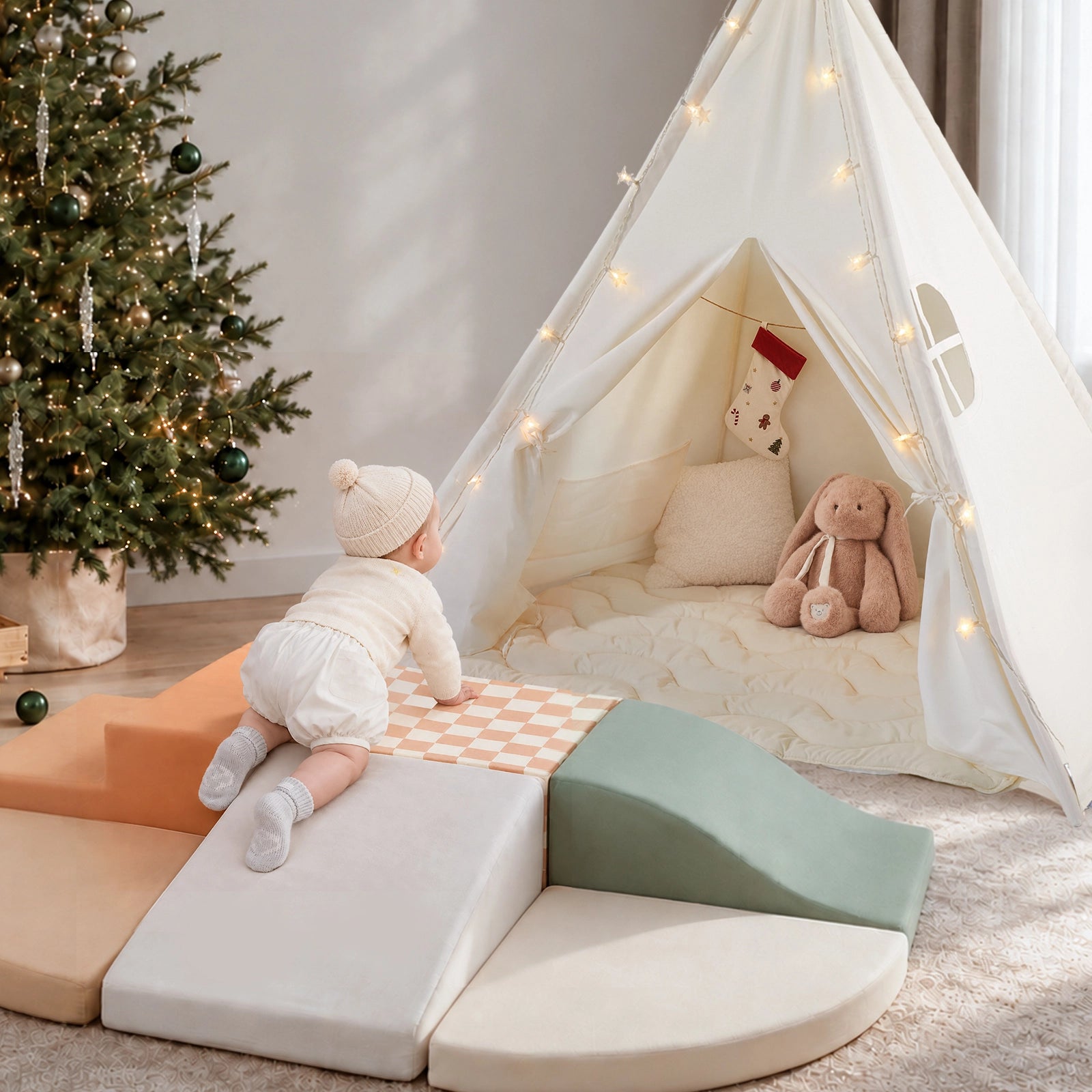 A baby in a knit hat crawls onto Tiny Land® Teepee Tent & PlayNest Climbing Blocks in front of a cozy play corner featuring a white fabric teepee decorated with string lights.