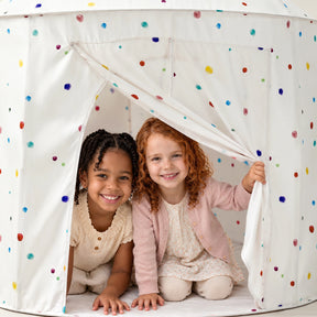 Two young girls smile while peeking out from inside a white polka-dot Tiny Land® Kids Tent – Indoor Tent for Toddlers.|Colorful Dots