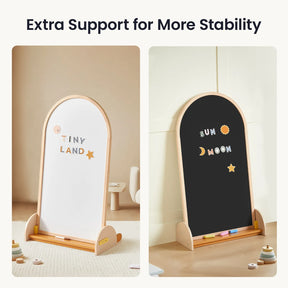 Two wooden-framed easels, including the Tiny Land® Double-Sided Arched Magnet Chalkboard & Art Kit—one side featuring a TINY LAND whiteboard and the other a SUN MOON chalkboard—stand in a light-colored room with toys and a small table in the background, making an ideal kids’ art easel or perfect addition to any child's art accessory collection from Tiny Land.